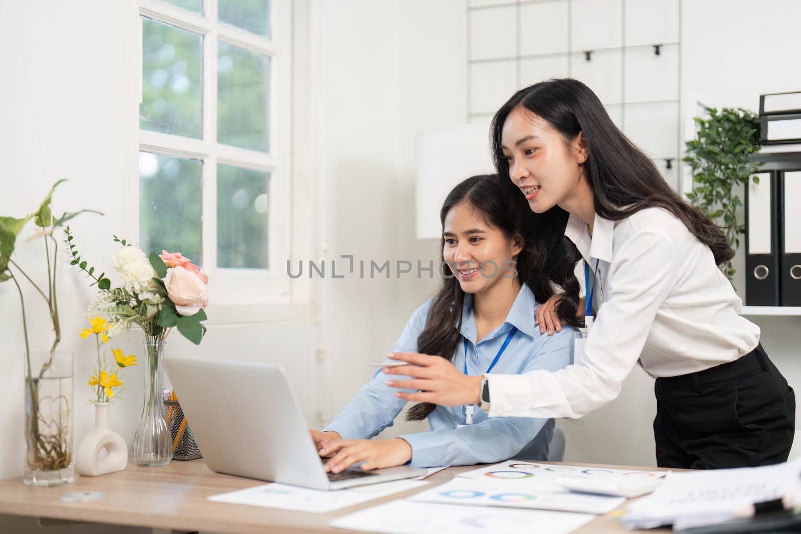 Two young women collaborating on a project, analyzing data and sharing insights in a modern office environment.