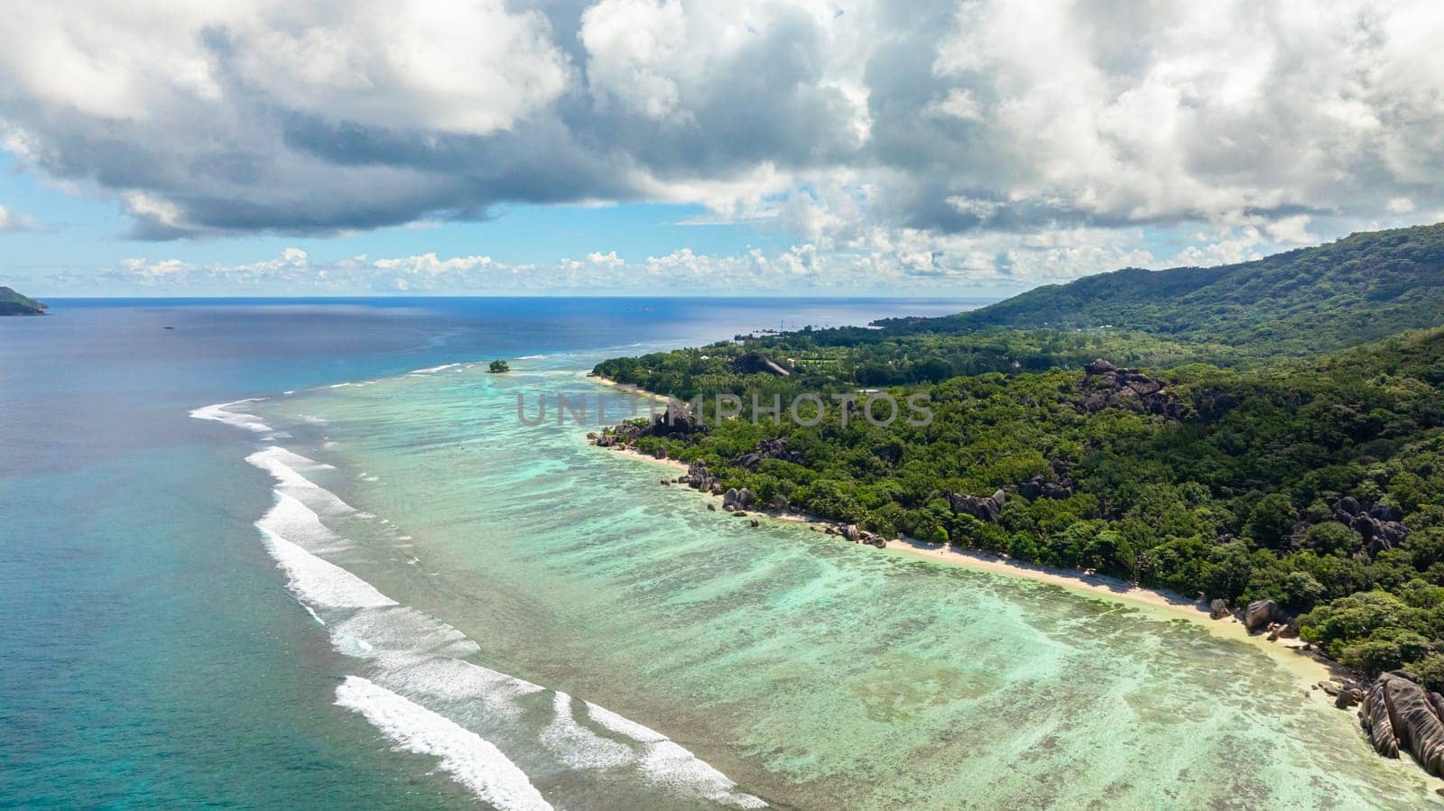 A secluded beach with crystal clear waters, surrounded by granite rocks and dense vegetation. Seychelles, La Digue.