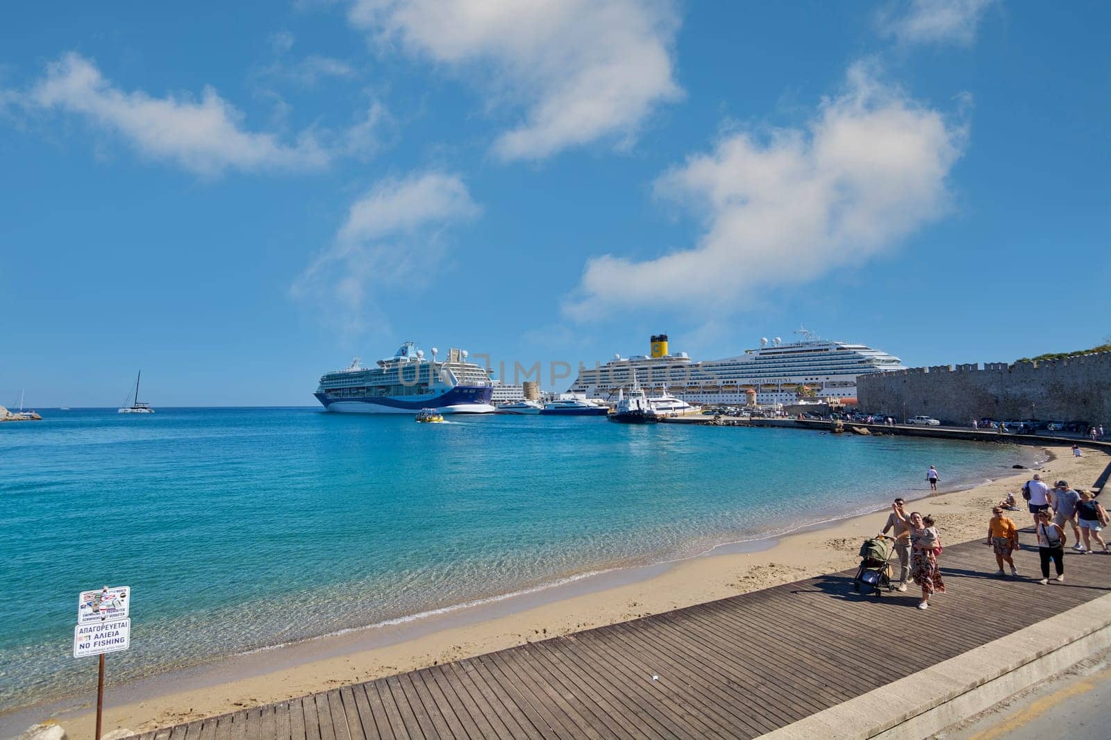 Rodas.Greece - june 06, 2025: Rhodes port with impressive cruise ships and a turquoise beach under a blue sky. Tourists enjoy the promenade on a sunny day, reflecting the relaxed atmosphere of the Greek island.