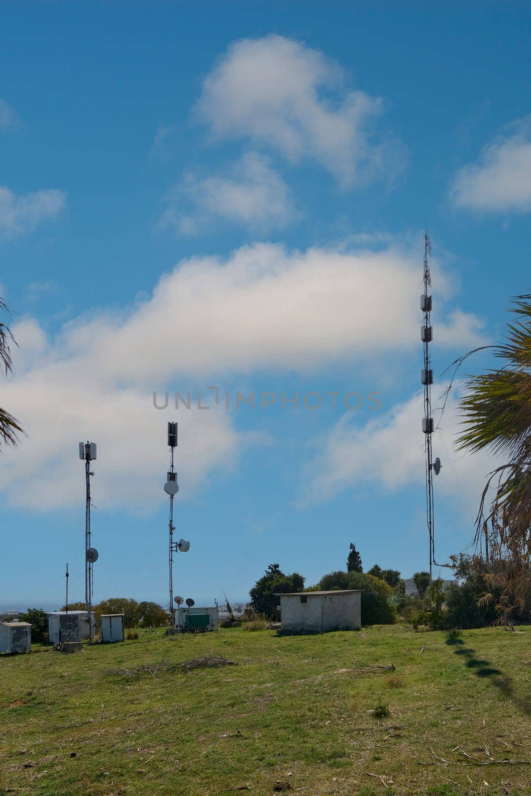A cluster of telecommunication towers stands in a green landscape in Rhodes, Greece, under a blue sky with clouds, representing modern connectivity.