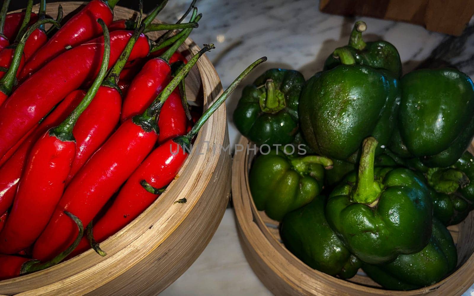 Vibrant red chili peppers and fresh green bell peppers arranged in bamboo bowls creating a colorful display perfect for food themes, cooking, healthy eating, and agricultural or culinary content.