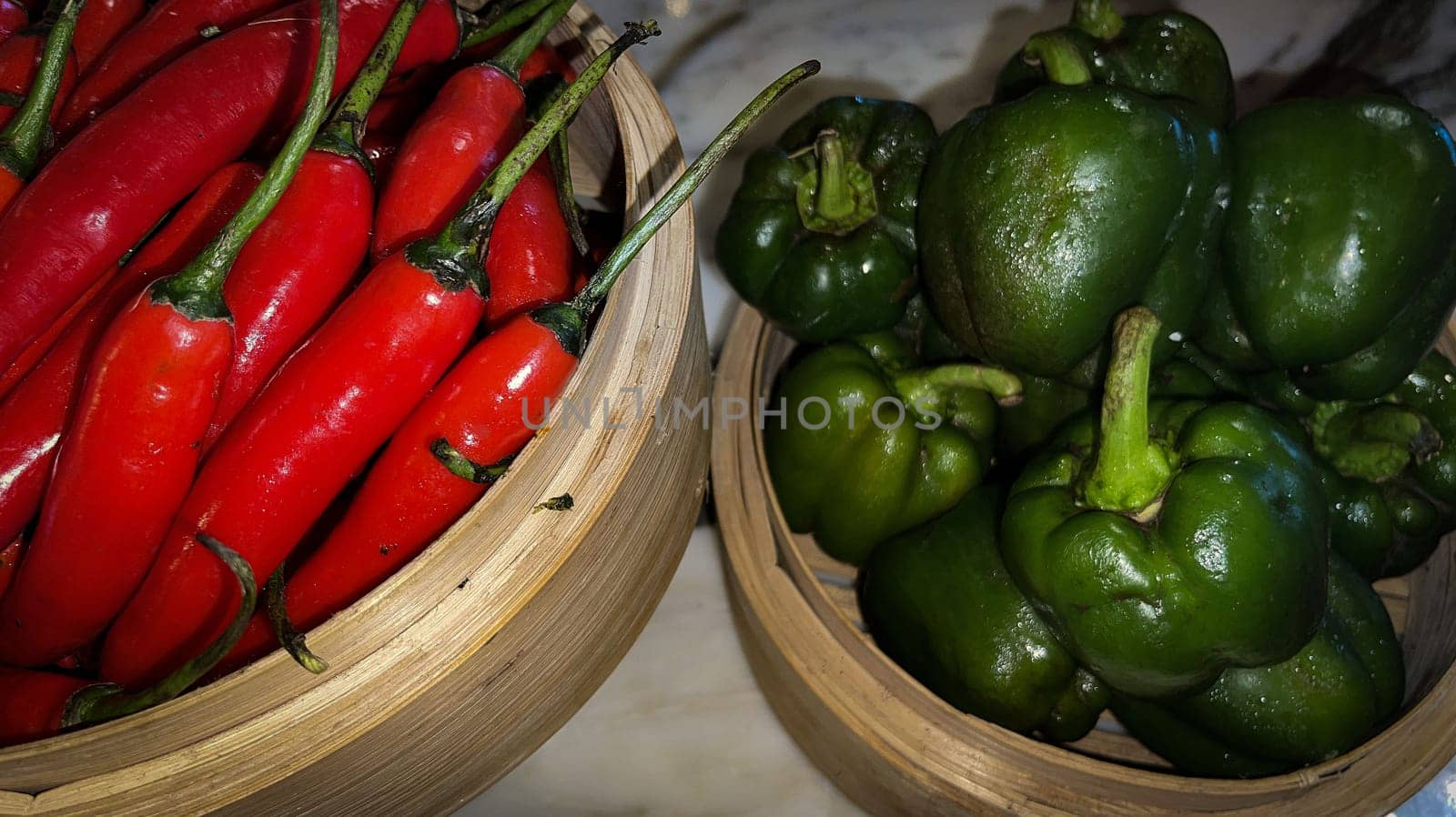 Vibrant red chili peppers and fresh green bell peppers arranged in bamboo bowls creating a colorful display perfect for food themes, cooking, healthy eating, and agricultural or culinary content.