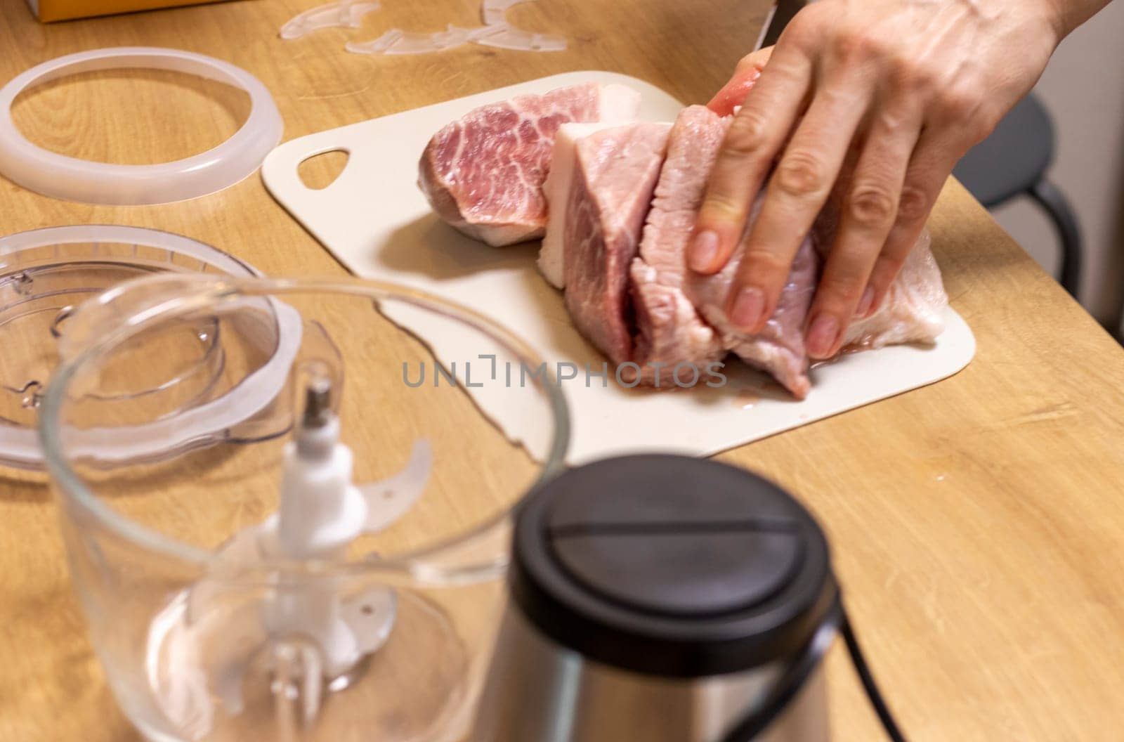 Woman cuts the meat, prepares it to grind it in electrical chopper