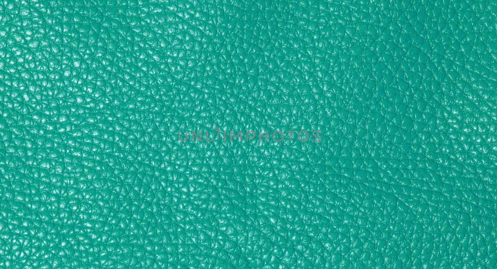 A close up full frame view of a vibrant teal colored leather texture, showcasing its natural grain