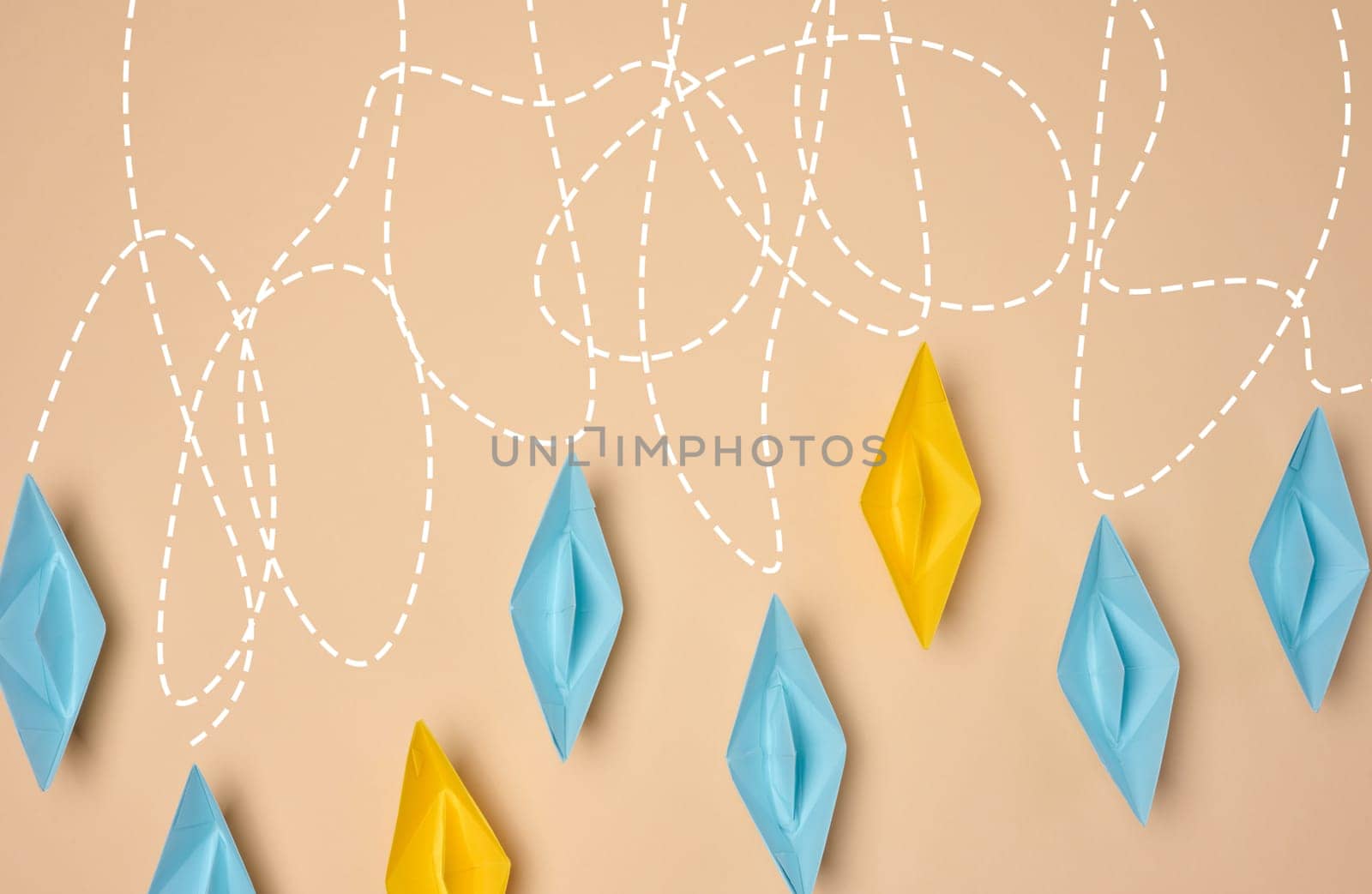 A creative composition featuring blue and yellow paper boats with dashed lines trailing behind them on a beige background, journey or exploration