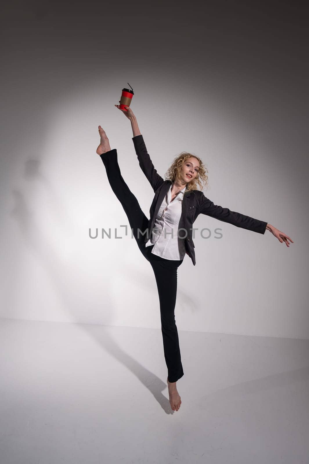 Barefoot ballerina in business suit dancing with a cup of coffee on a white background