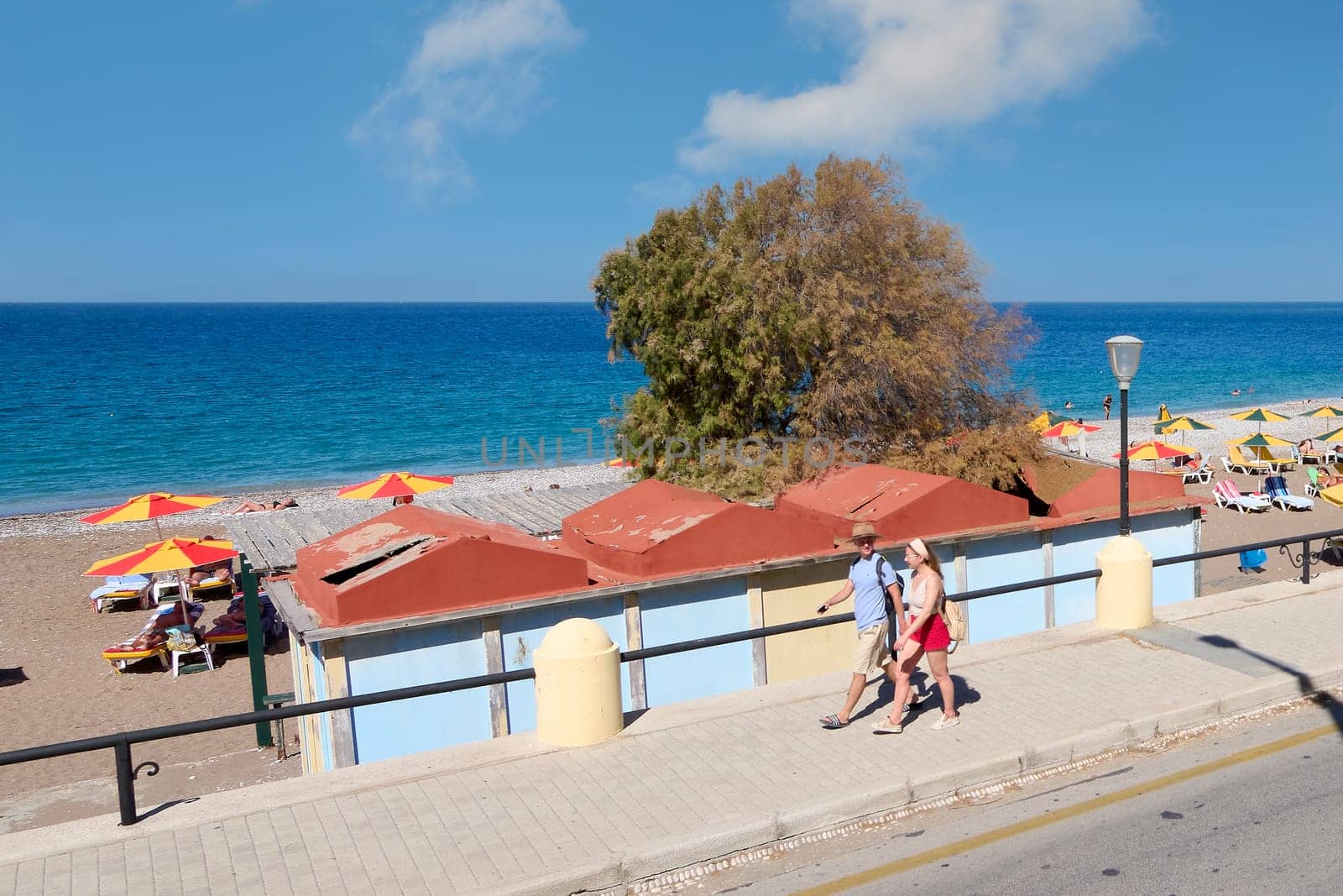 Rodas.Greece - june 07, 2025: An idyllic beach scene in Rhodes, where people relax under yellow and green umbrellas, with the vast and serene Aegean Sea as a backdrop