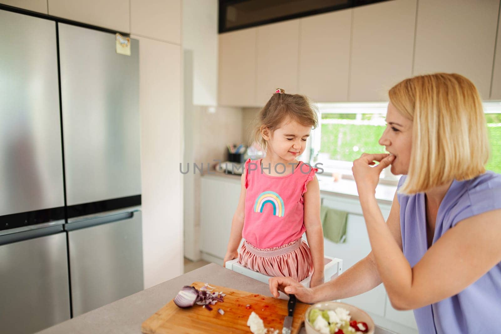 Child enjoys cooking with parent in a bright kitchen.