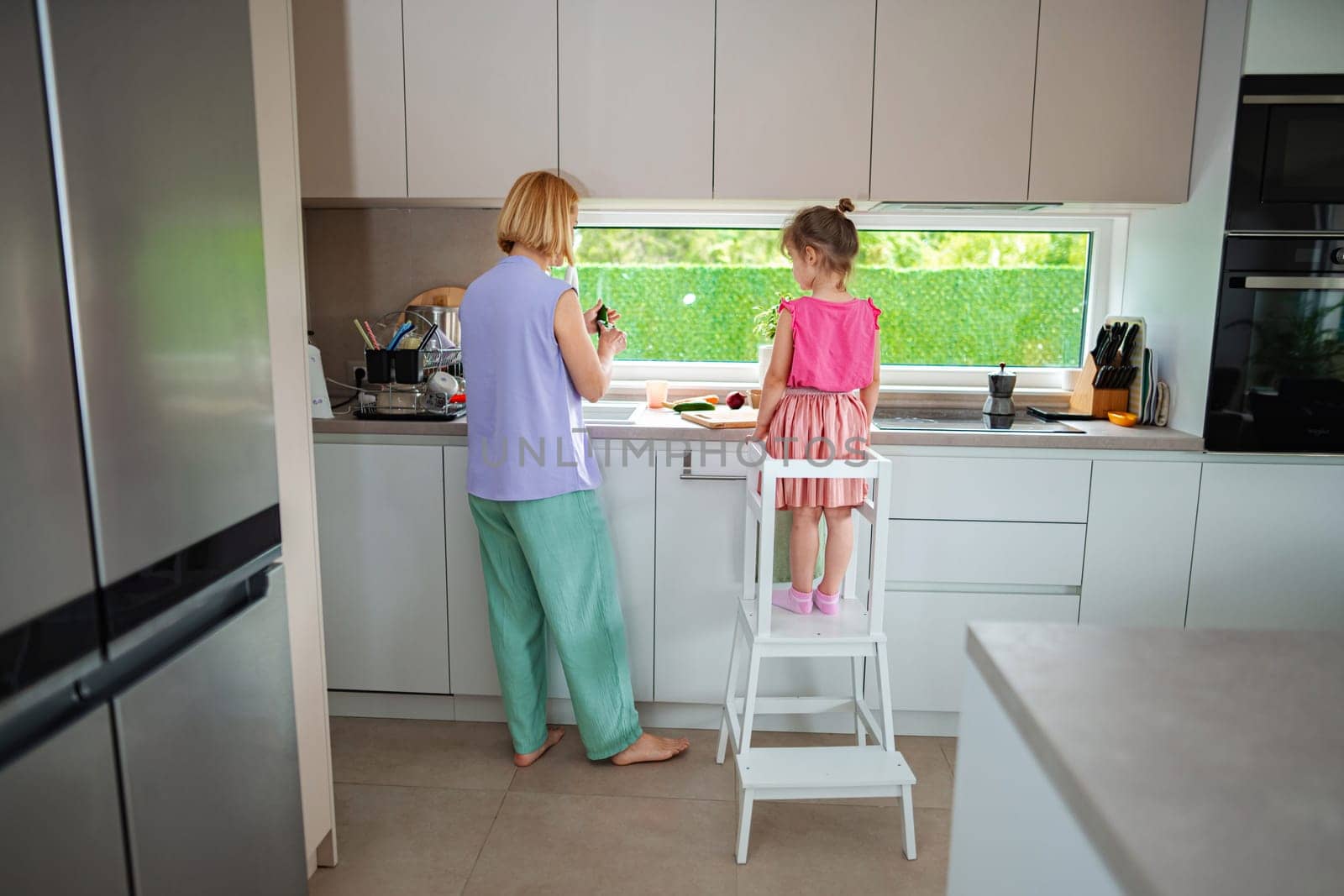 Mother and daughter enjoy preparing food in a bright kitchen.