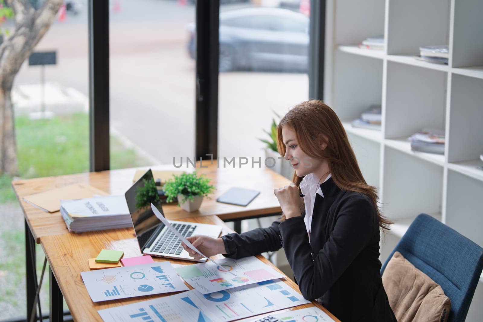 Young businesswoman analyzes charts and graphs at her office desk carefully..