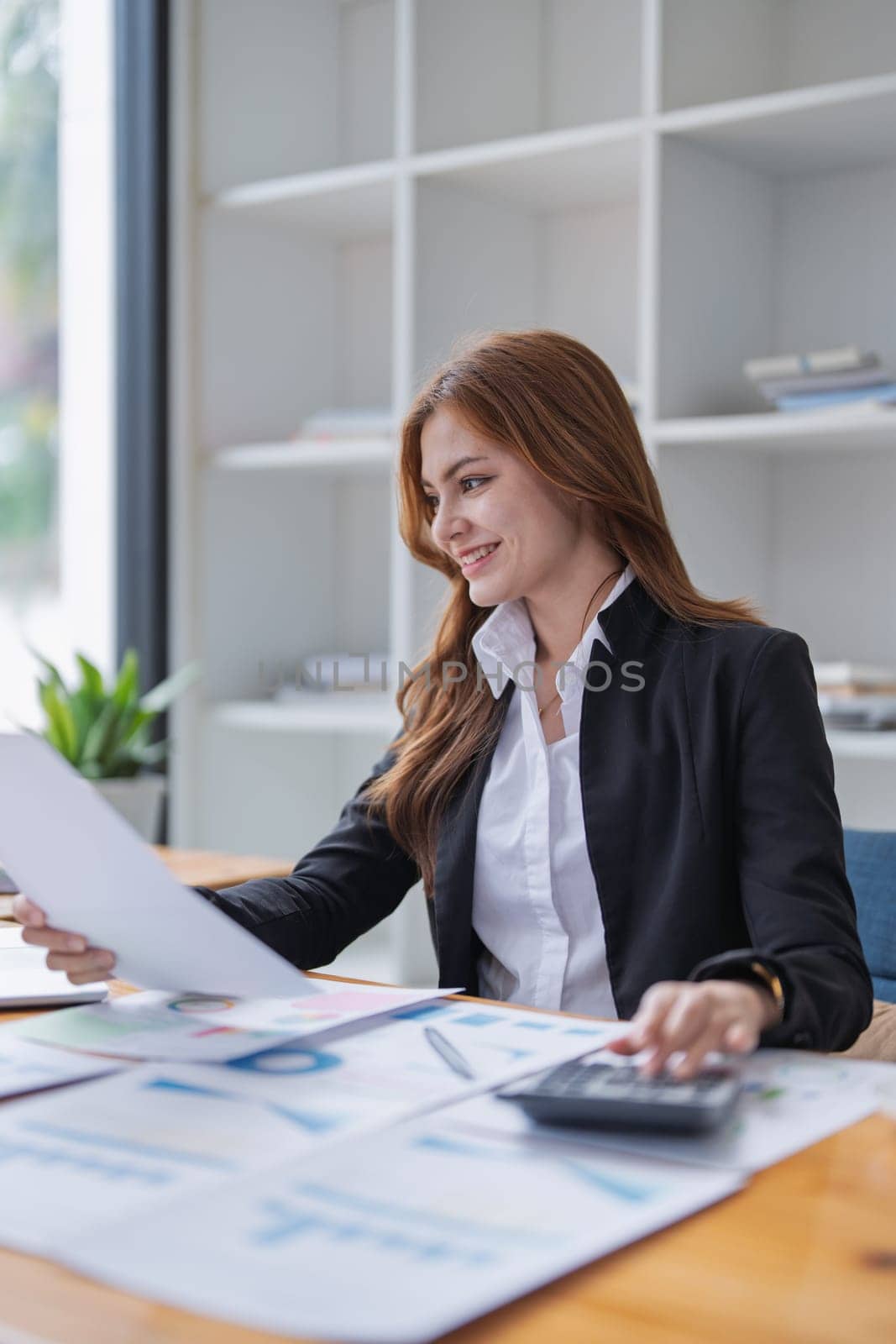Attractive woman reviews financial documents and calculates figures at desk..