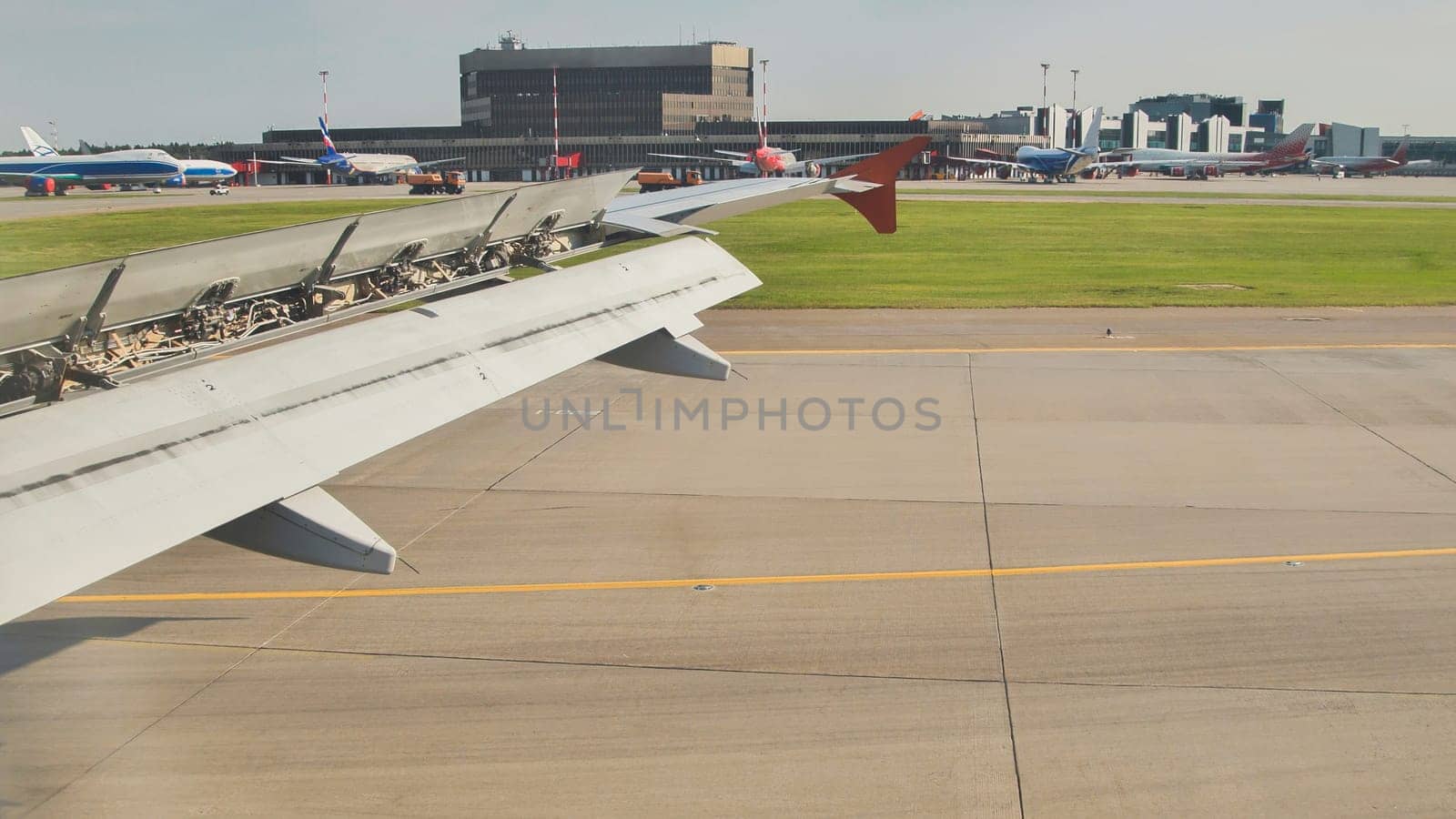 Airplane wing over airport runway during landing maneuver with deployed flaps and spoilers