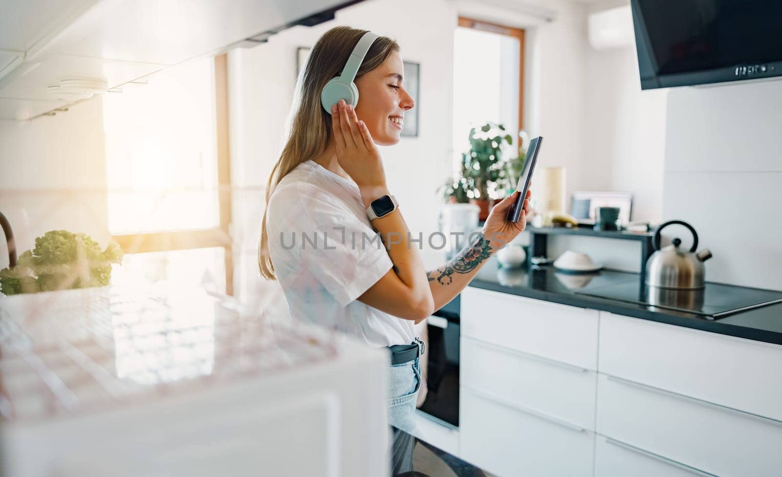 A woman with headphones is engaged with her tablet in a stylish kitchen, showcasing a modern lifestyle