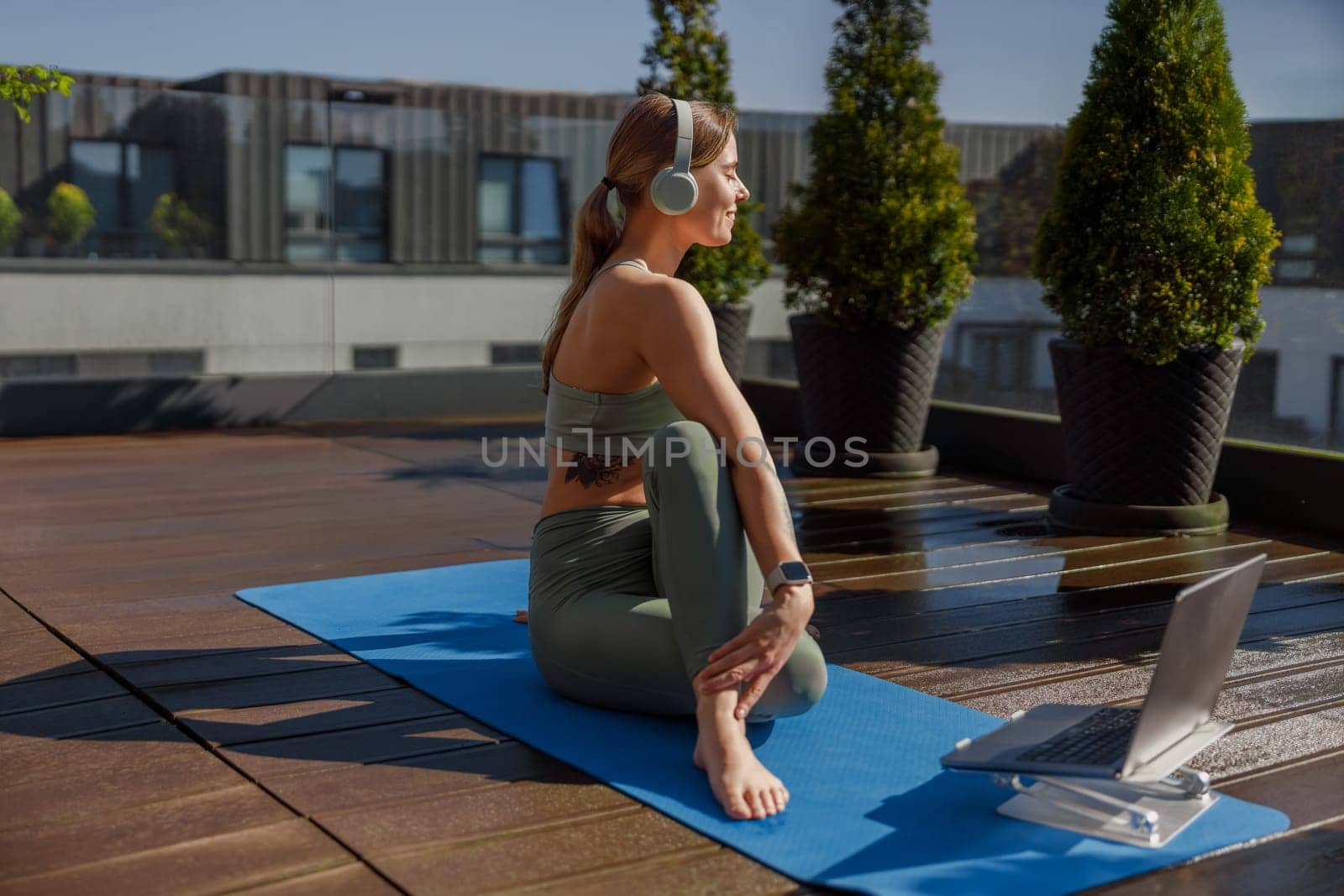 A focused woman practicing yoga outdoors on a sunny rooftop, harmoniously blending relaxation and modern technology