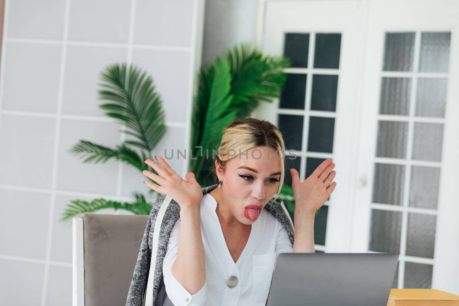 Business woman sitting at office desk with laptop and sticking out her tongue