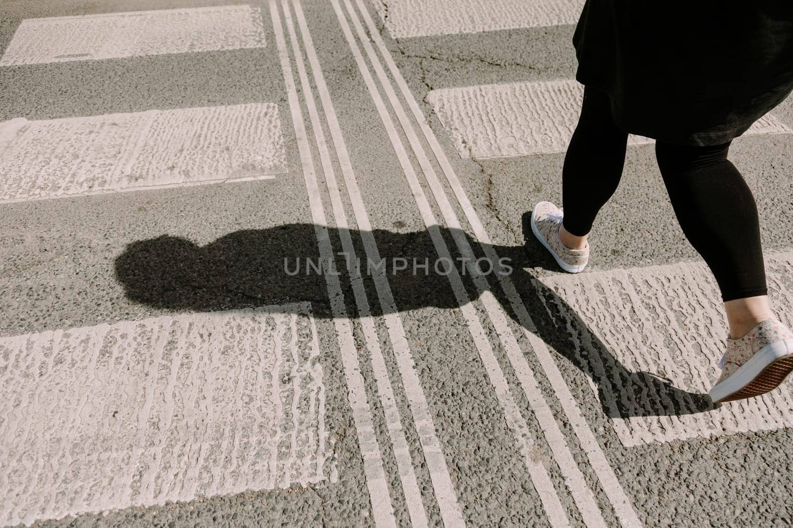 A woman confidently striding over a city crosswalk, captured from behind in bright sunlight. Perfect for themes of personal journey, direction, motivation, and lifestyle in urban settings