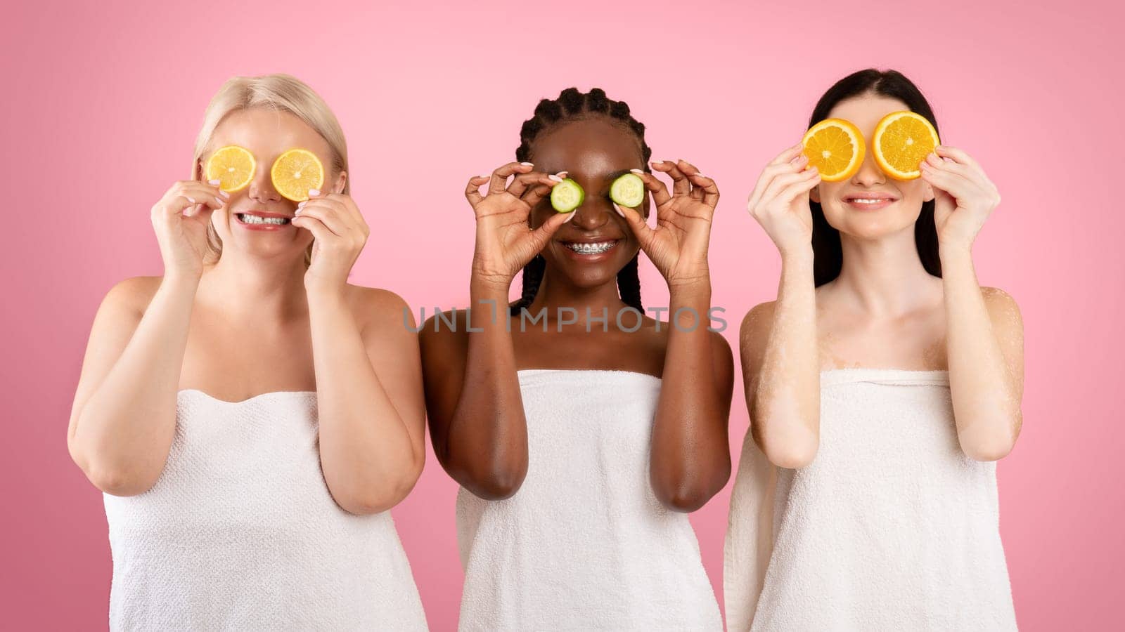 Beauty And Skin Care. Three Diverse Women In Bath Towels Covering Eyes With Cucumber And Orange Slices, Making Organic Face Masks, Posing Together Over Beige Studio Background, Copy Space