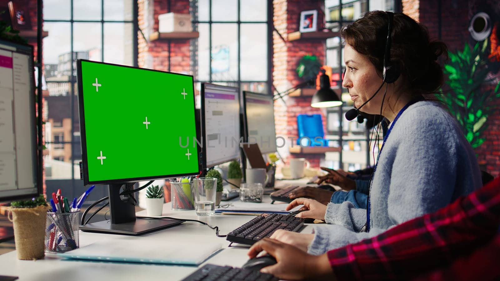 Call center employee working on green screen mockup PC, doing account management in office. Customer support agent in front of chroma key isolated screen computer handling calls, camera B close up
