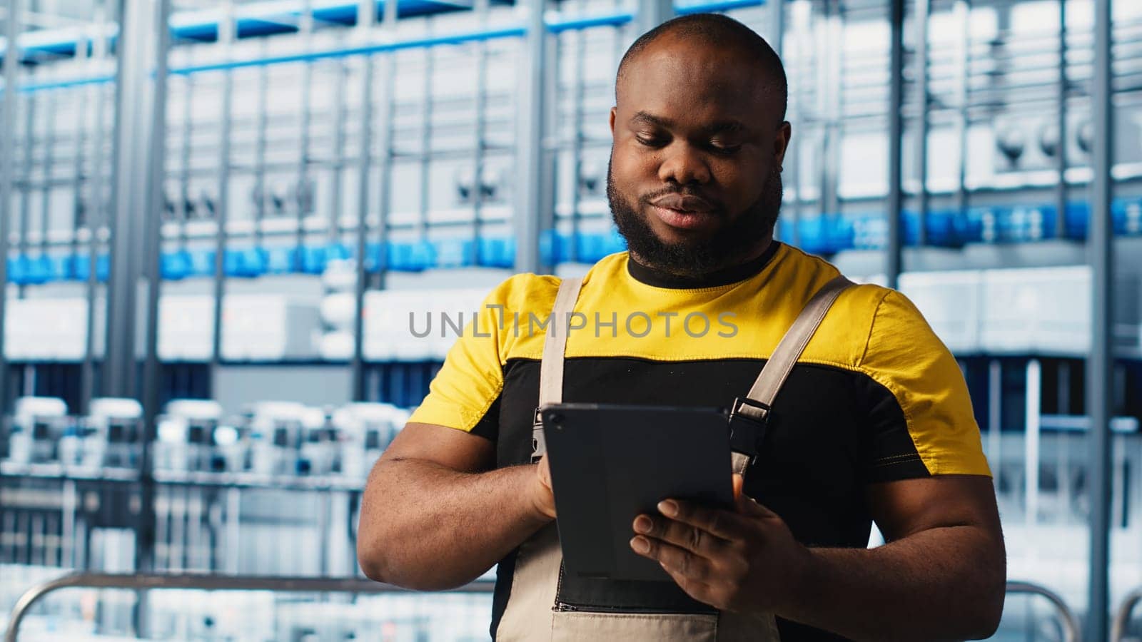 Smart factory engineer oversees operation of robotic arms and assembly lines on facility floor. Industry 4.0 plant african american man monitors system performance and troubleshoots issues, camera A