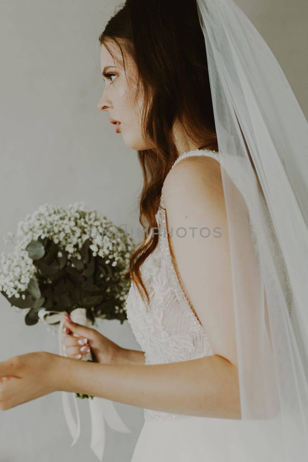 Portrait of one beautiful young Caucasian recognizable brunette bride holding a bouquet of white boutonnieres and waving her arms with serious emotion on her face, bottom view close up with selective focus.