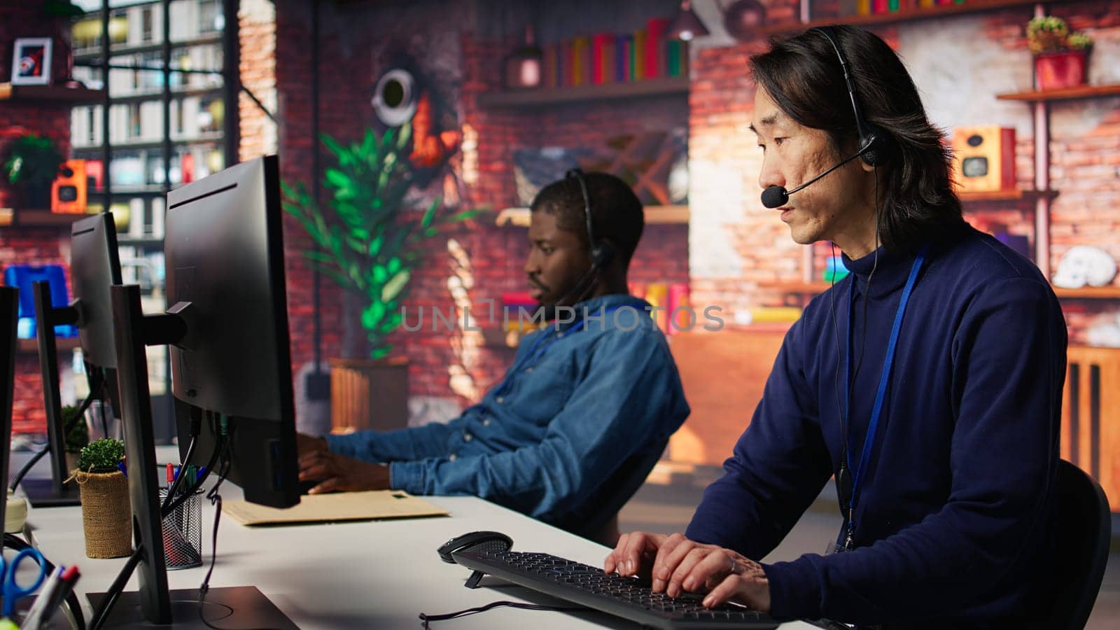 Call center senior agent dealing with unhappy customers, listening to issues. Experienced Asian customer support worker handling clients complaints in company workspace, camera B