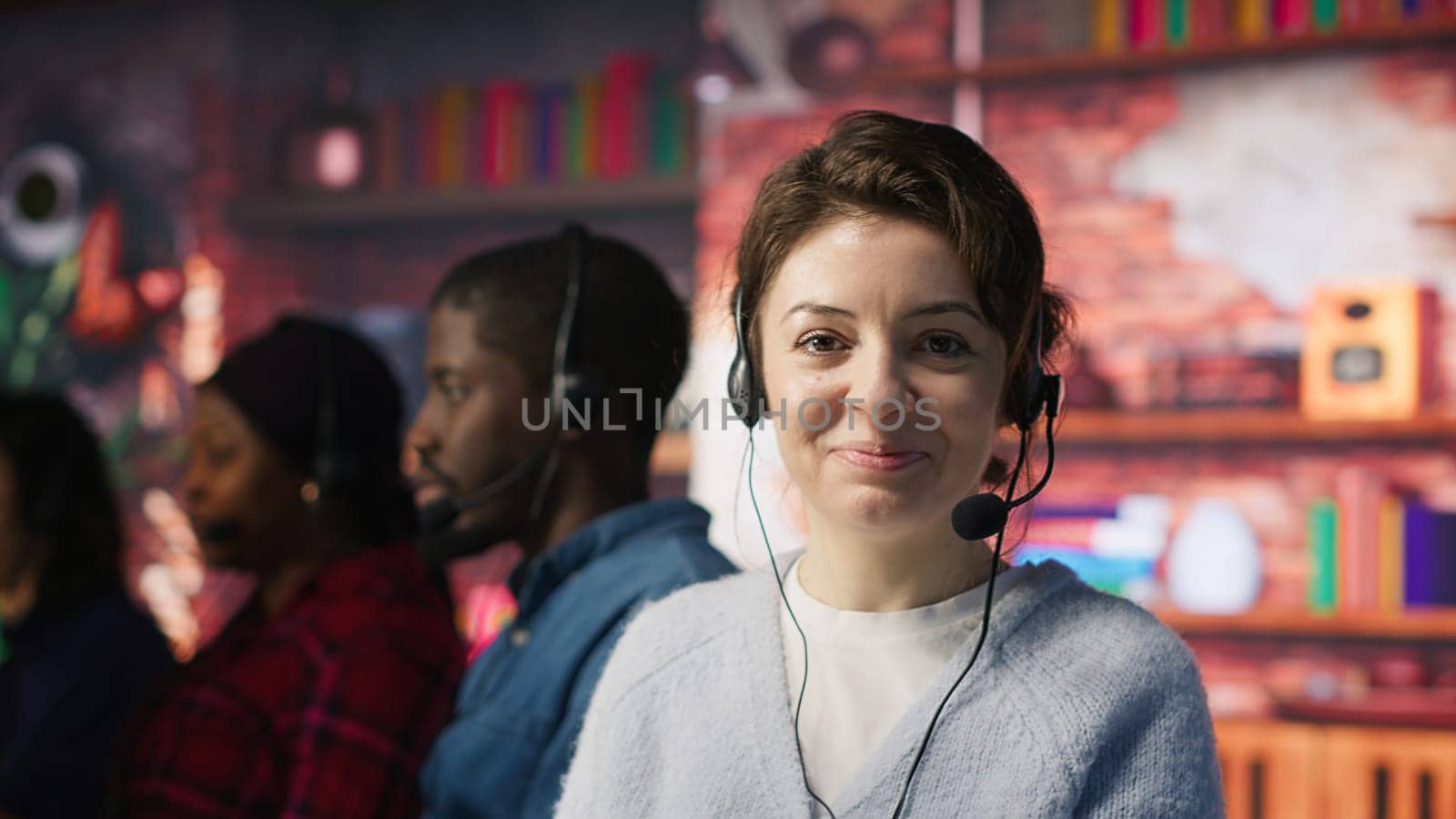 Cheerful call center employee wearing audio headset assisting customers in office. Upbeat woman at work doing customer support, communicating with clients in telephone call, camera A close up