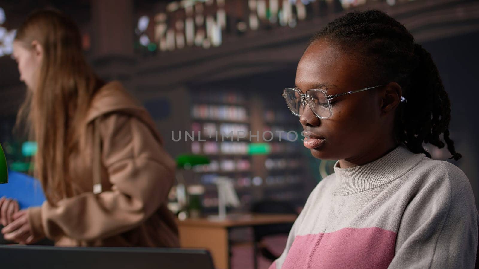 Black girl studying in university library for her bachelor degree diploma, using the educational research collection and general database for knowledge. Collecting citations for paper. Camera B.