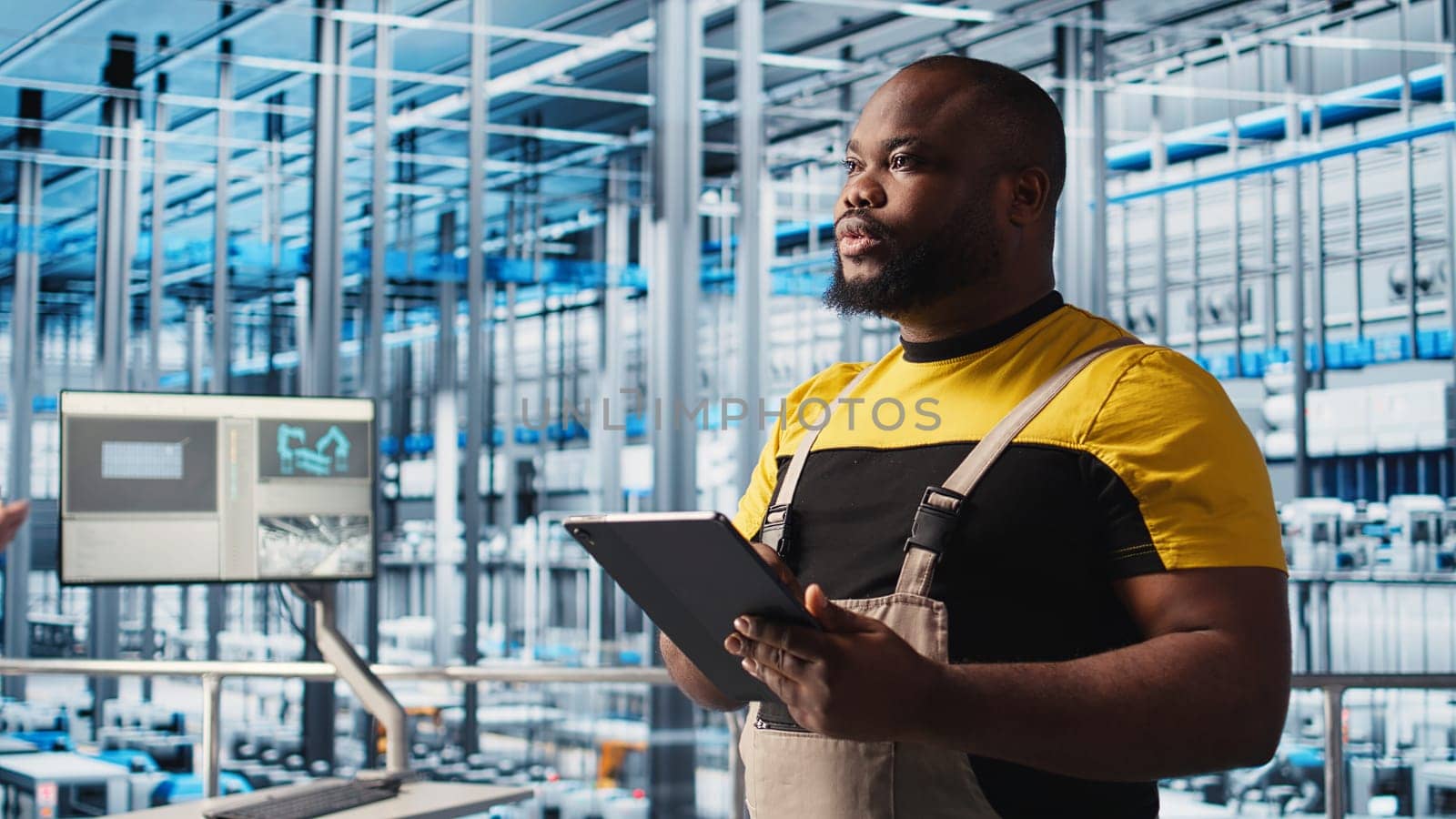 Smart factory engineer oversees operation of robotic arms and assembly lines on facility floor. Industry 4.0 plant african american man monitors system performance and troubleshoots issues, camera A