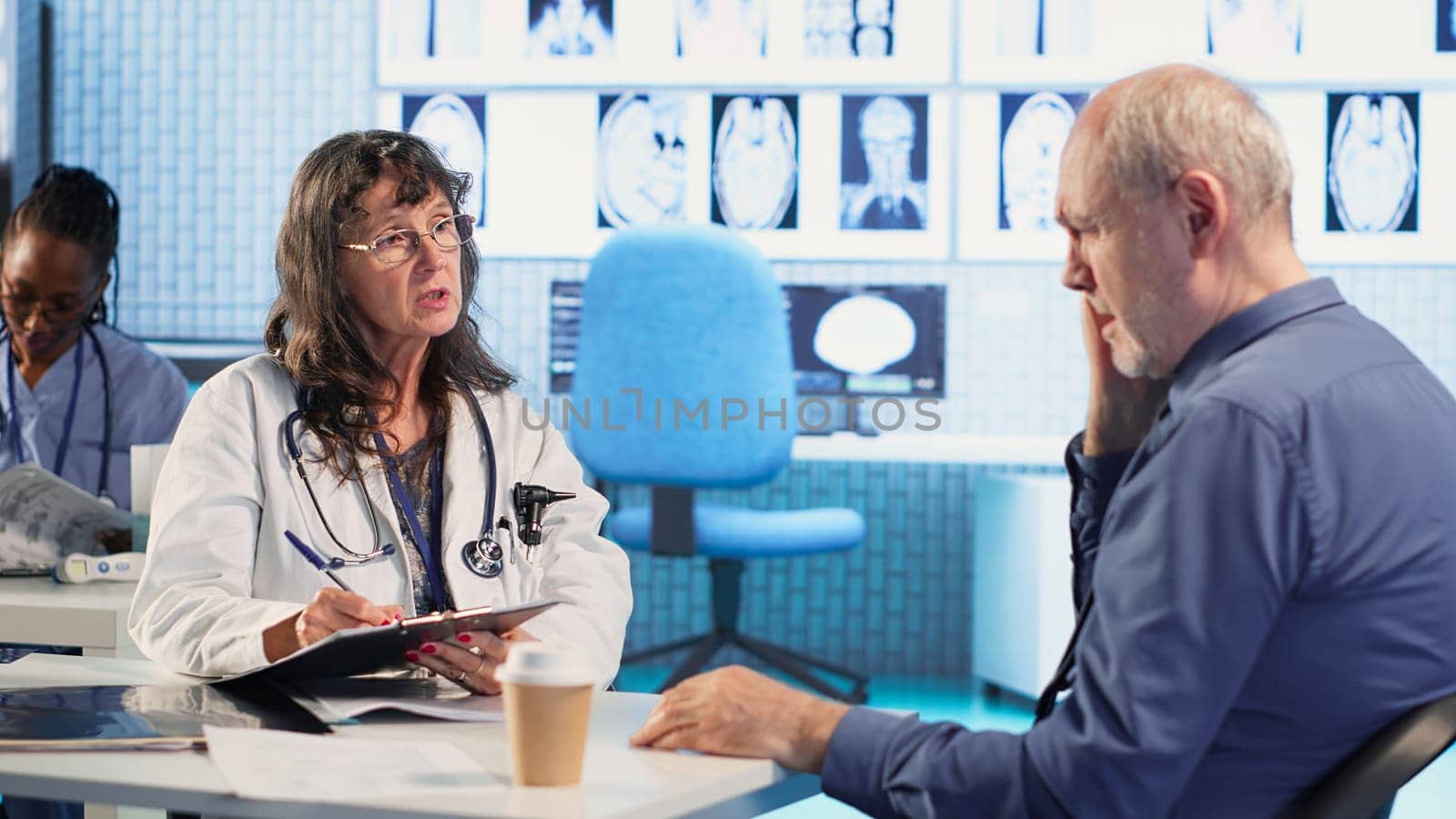 Female doctor providing expert advice to cure a migraine during checkup. Medic consulting a elderly patient in a modern cabinet with radiology reports and painkillers on prescription. Camera B.