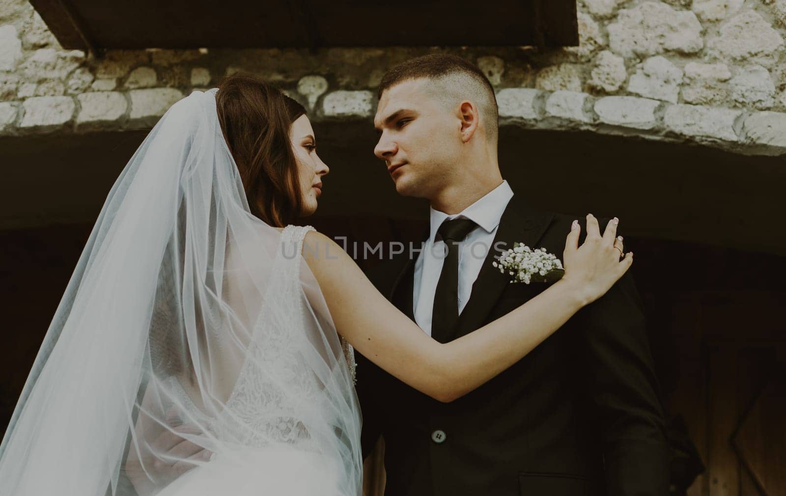 Young handsome Caucasian brunette couple of groom and bride looking at each other with love, holding each other by the shoulders and waist, standing on the steps at the entrance to the wedding castle on a cloudy rainy day, bottom side view close-up with selective focus.
