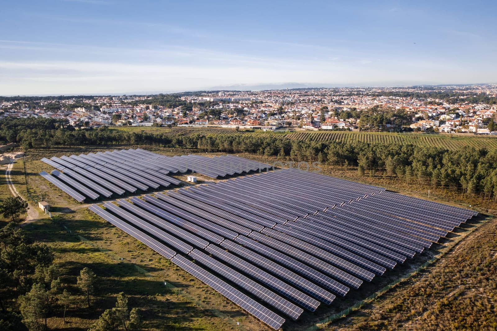 Aerial drone view of solar panels in fields, generating sustainable energy with a scenic townscape and sunny sky in the background
