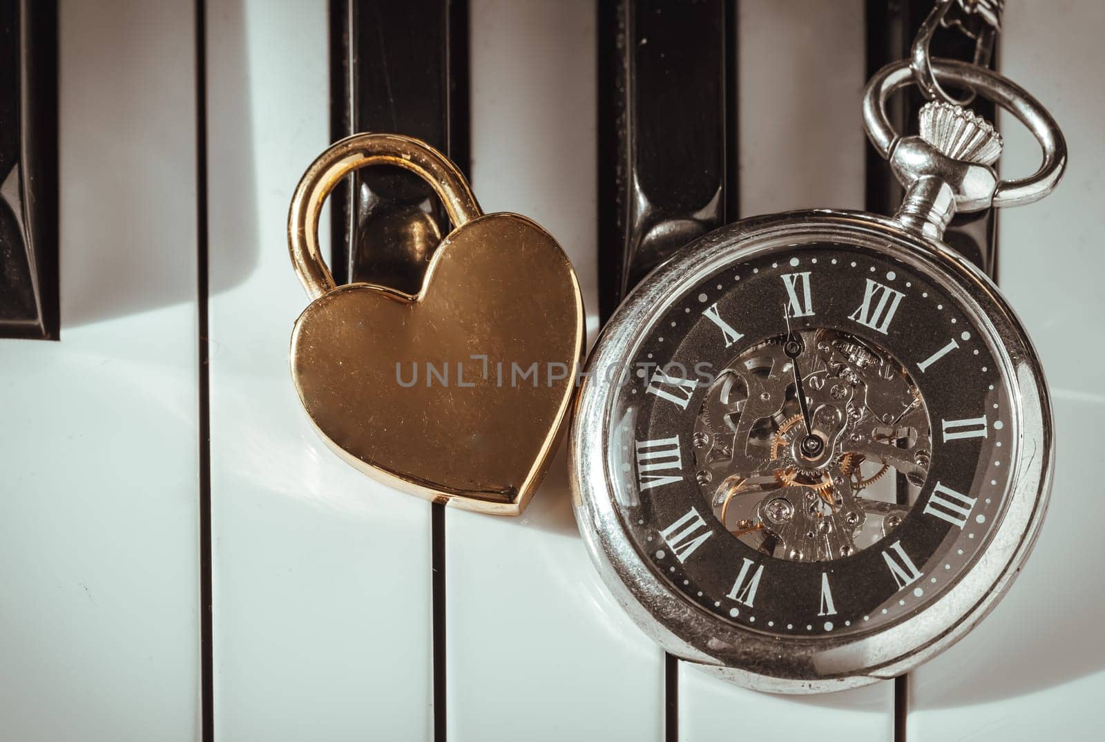 London, UK - Apr 19, 2025 - Top view of A retro pocket watch or Antique pocket watch with Golden heart shaped love padlock on Piano keys background in Vintage tone. The concept of the time of love, use it as your Wallpaper, Poster and Copy space, Selective focus.