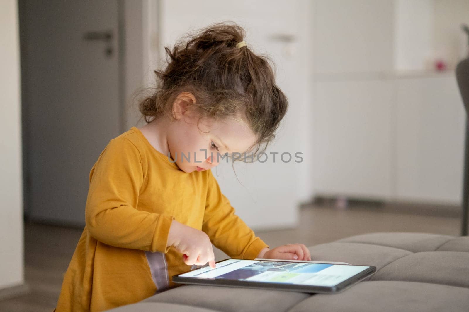Child engaged in creative activity, drawing on a touchscreen tablet. Living room with soft lighting and comfortable interior.