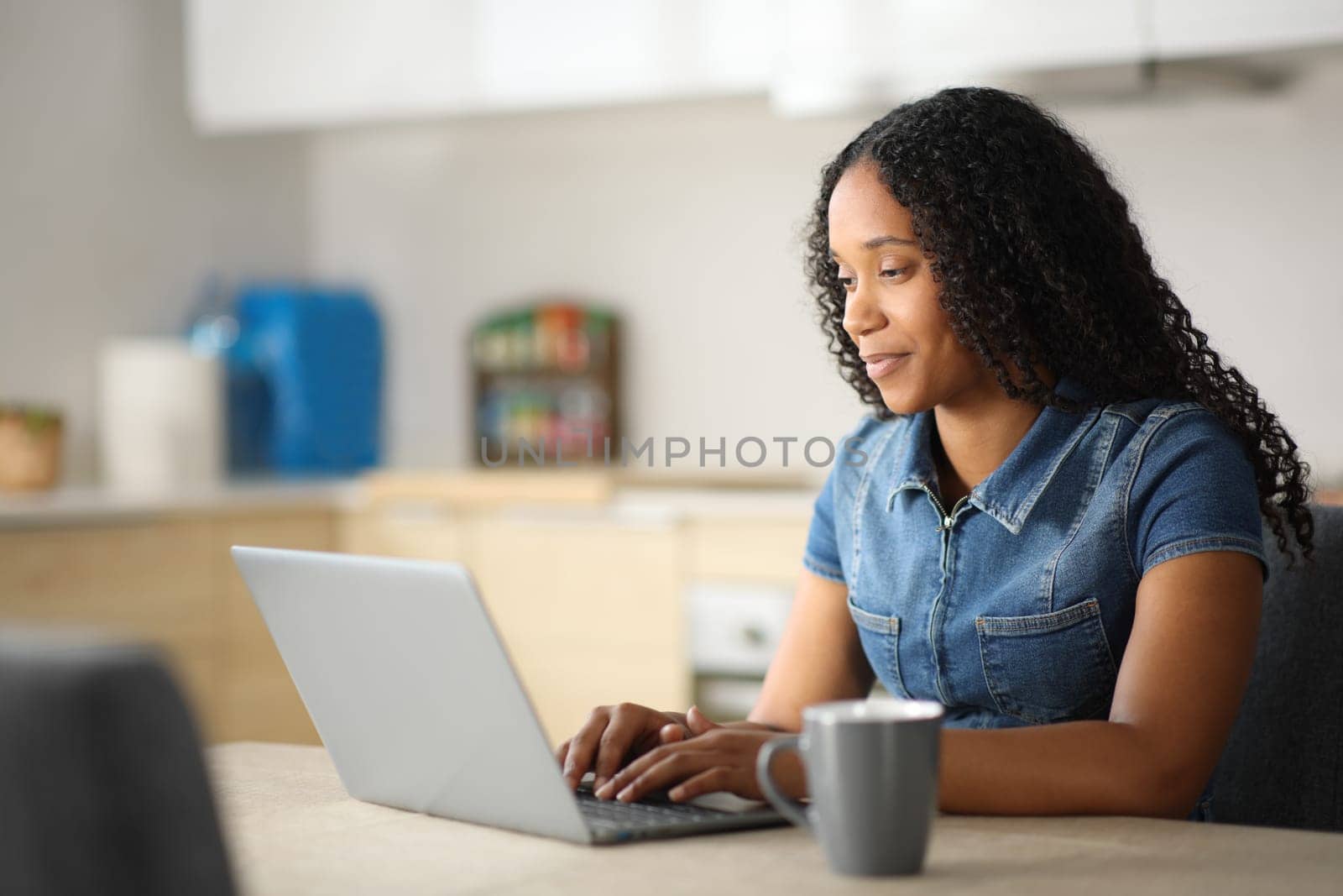 Black woman in a kitchen using laptop at home