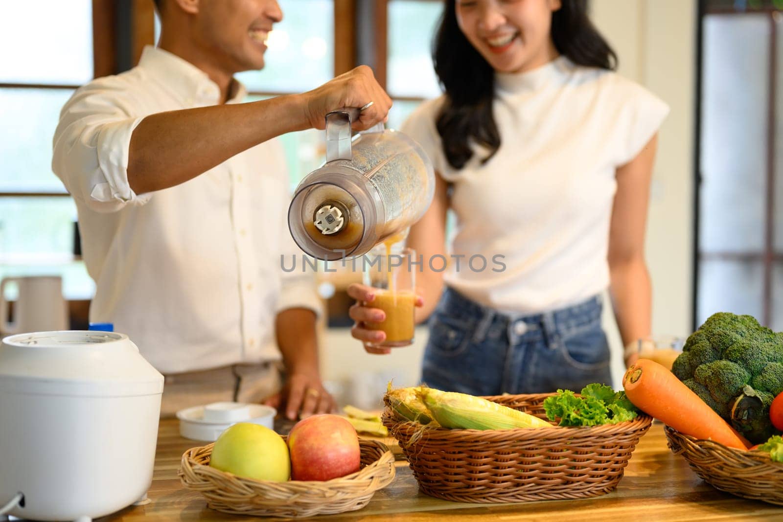 Smiling couple pouring fresh blended smoothie into a glass in a cozy kitchen.