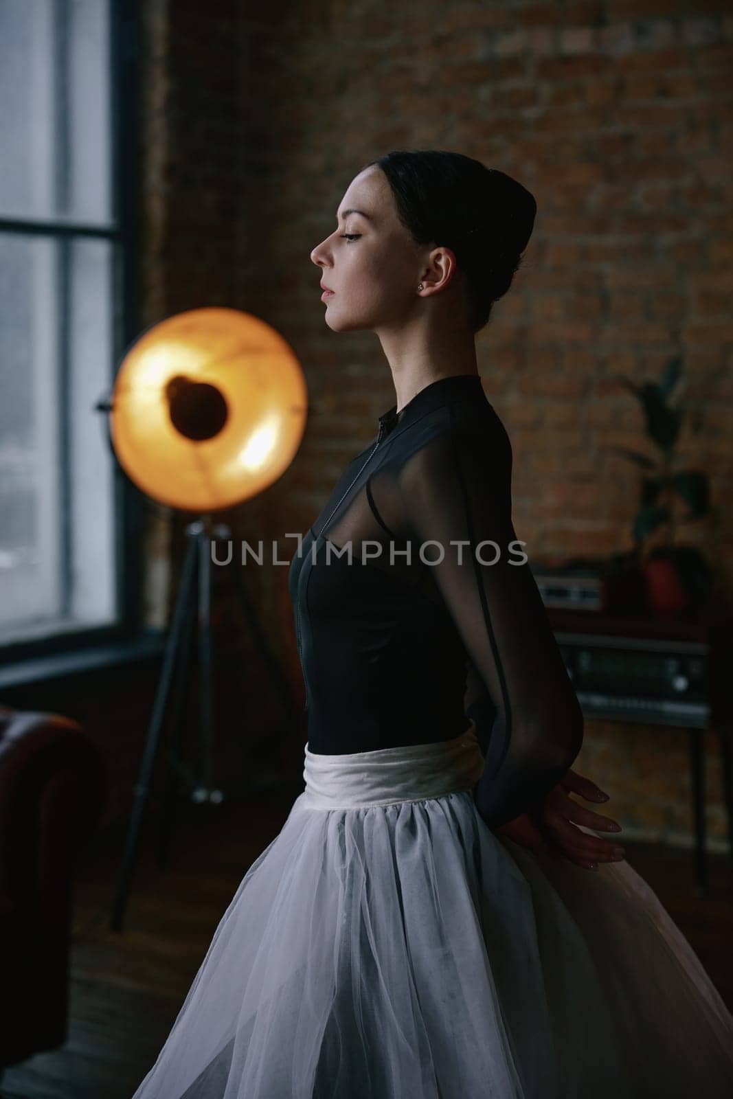A graceful ballerina delicately poses in a stylish loft featuring minimalist decor and dramatic lighting effects