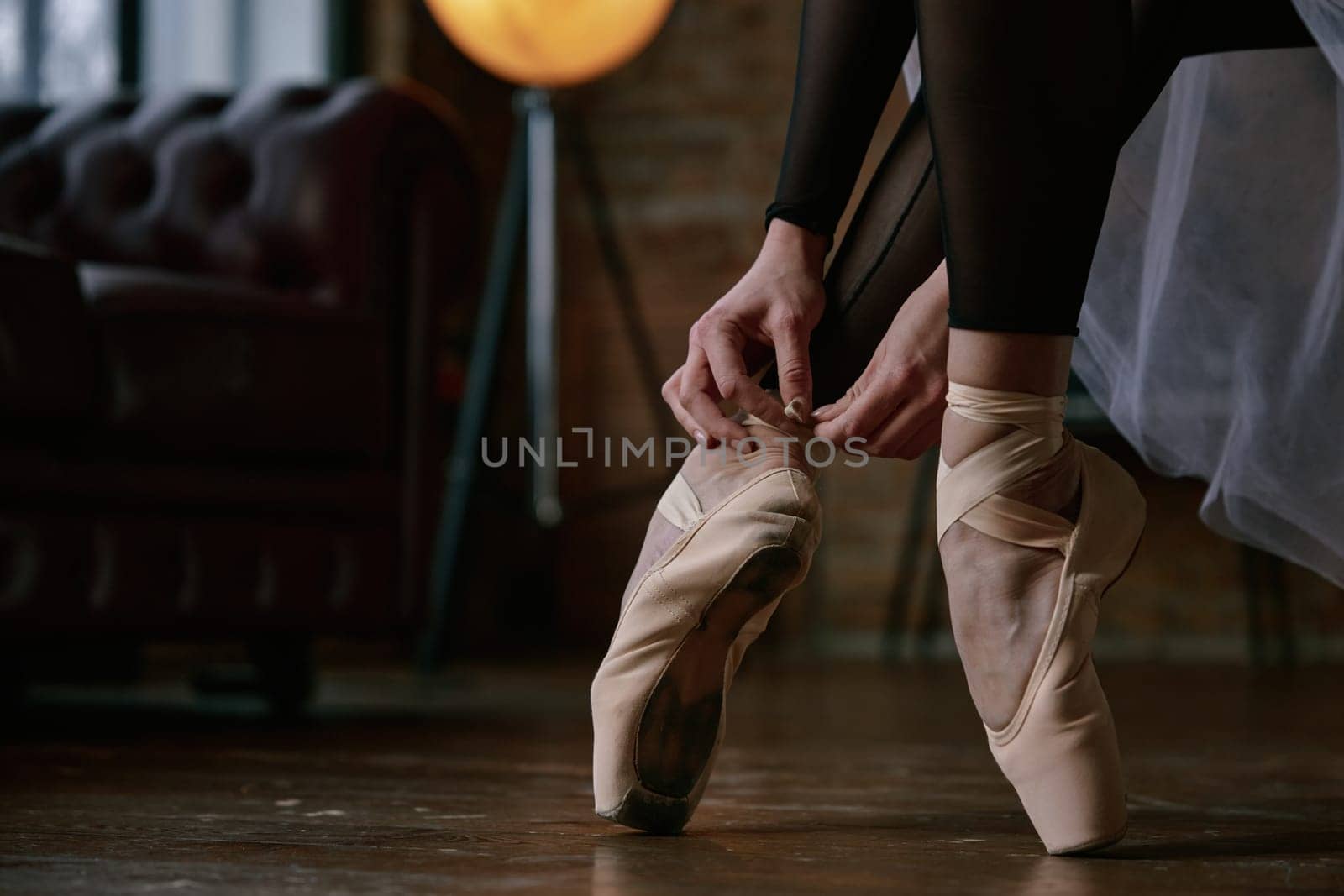 Crop shot of ballerina is gently and delicately wearing her ballet shoes inside a beautifully stylish studio ambiance