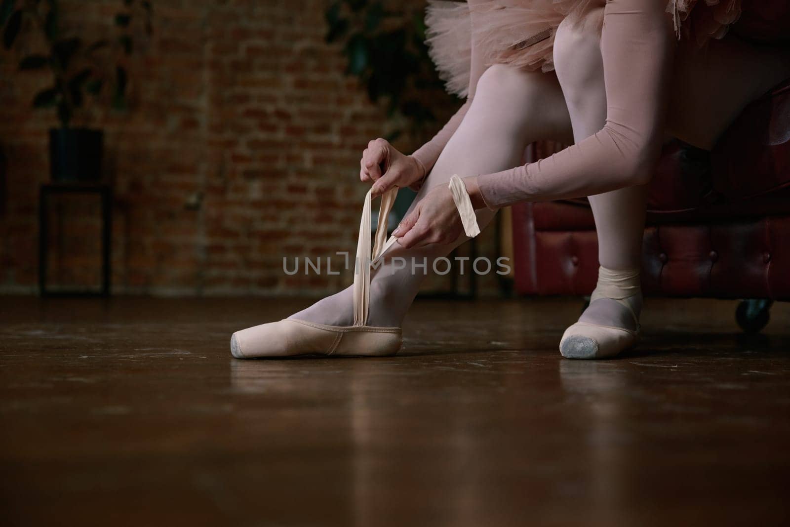 Ballerina is gently and delicately wearing her ballet shoes inside a beautifully stylish studio ambiance