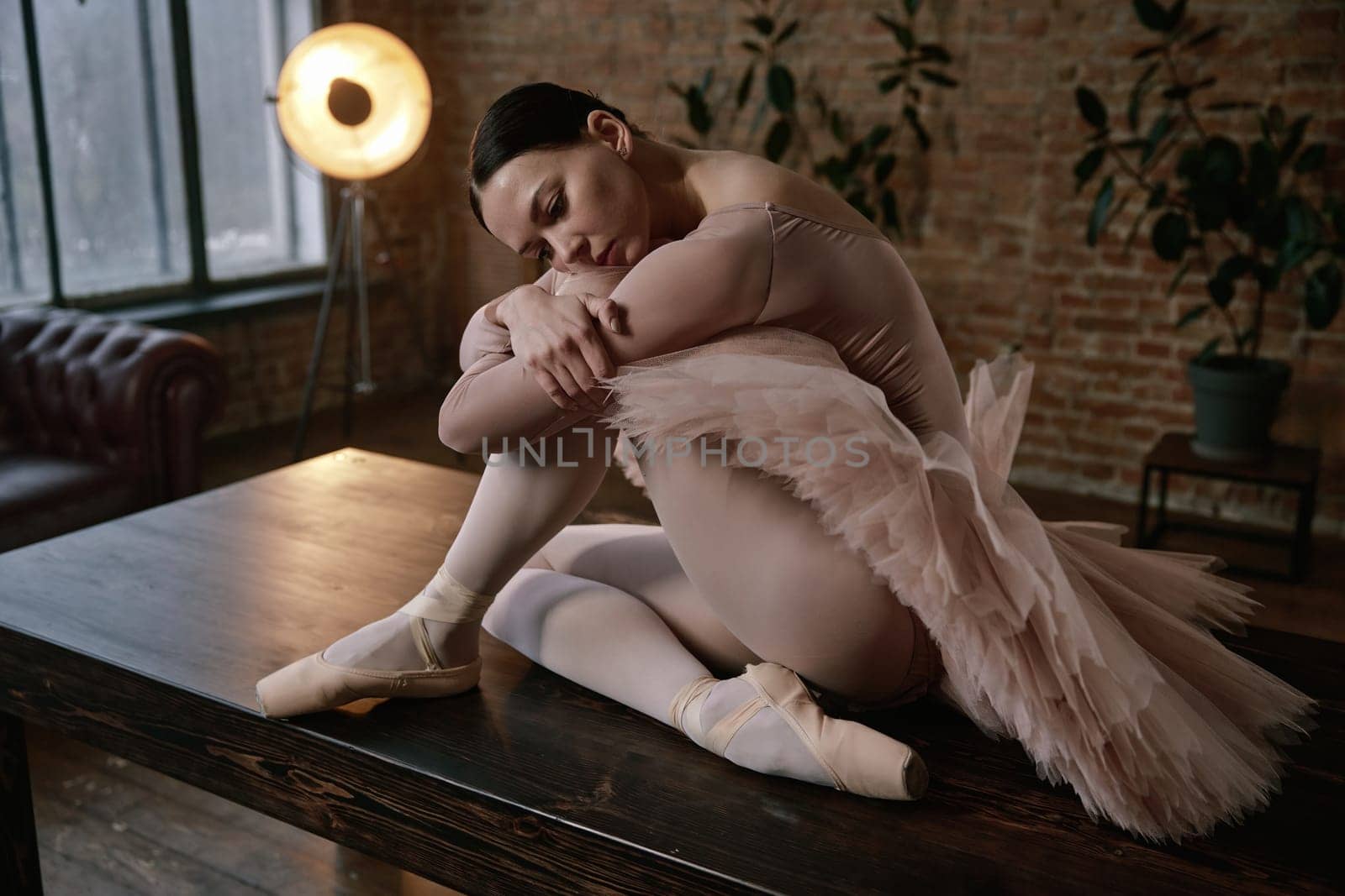 A ballerina in a pink tutu poses gracefully on a wooden table in a softly lit room, enhancing the ambience