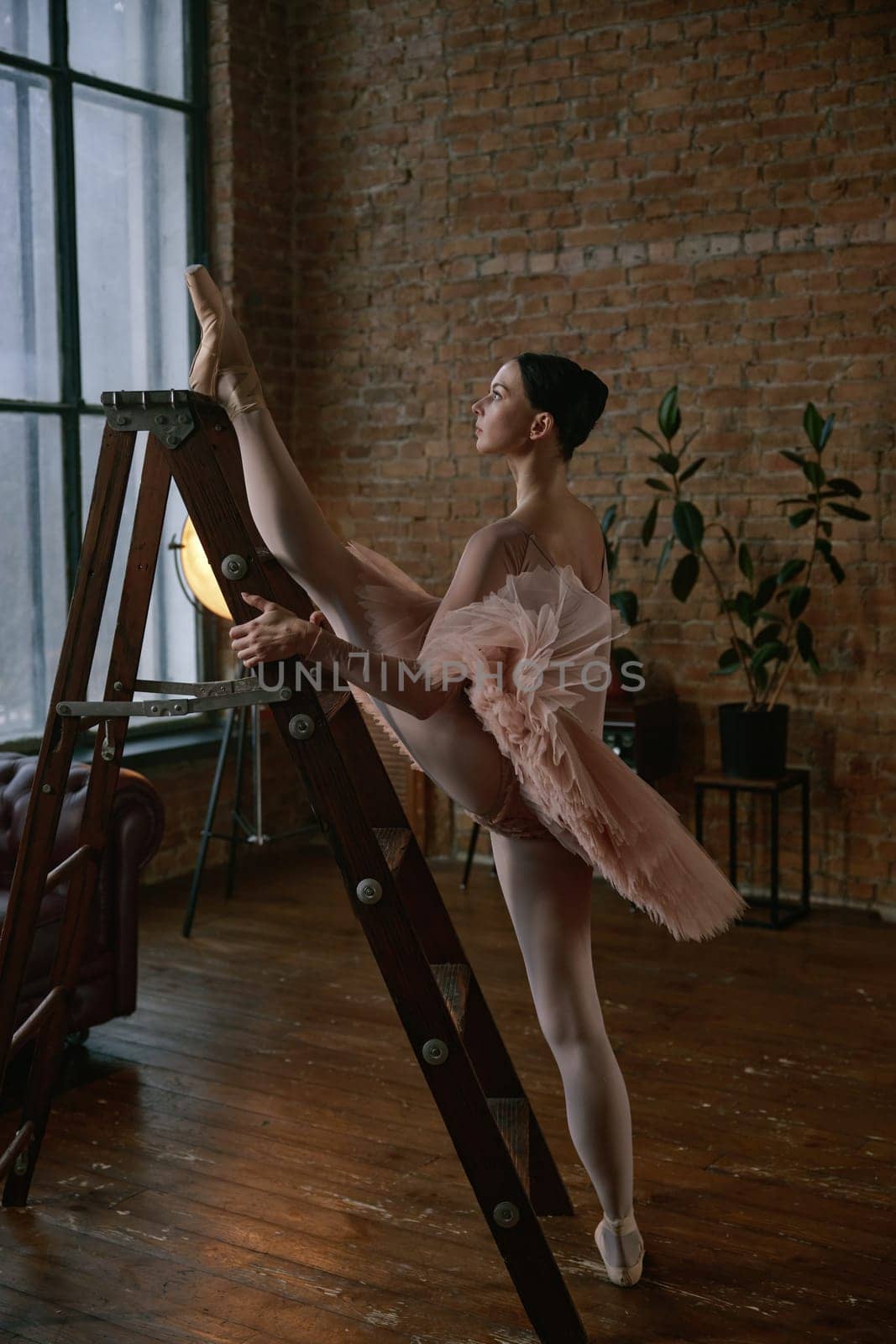 A ballet dancer showcases elegance and flexibility while stretching on a ladder in a stylish studio.