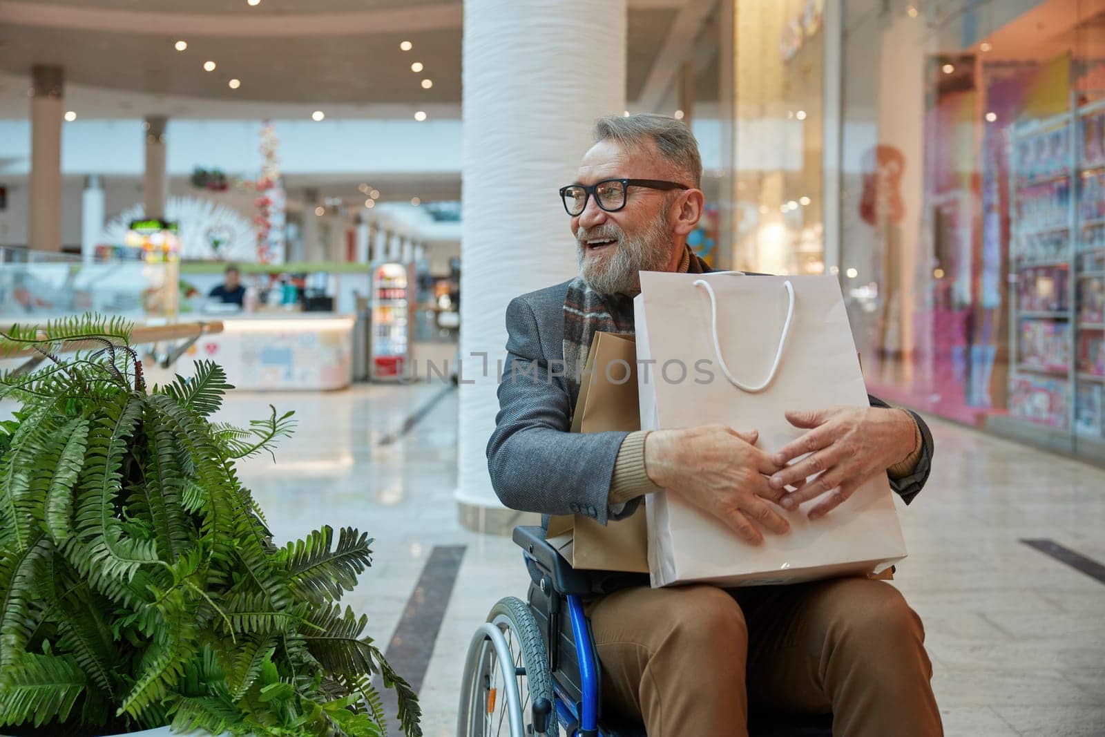 A man who is seated in a wheelchair holding shopping bag while moving through bustling mall filled