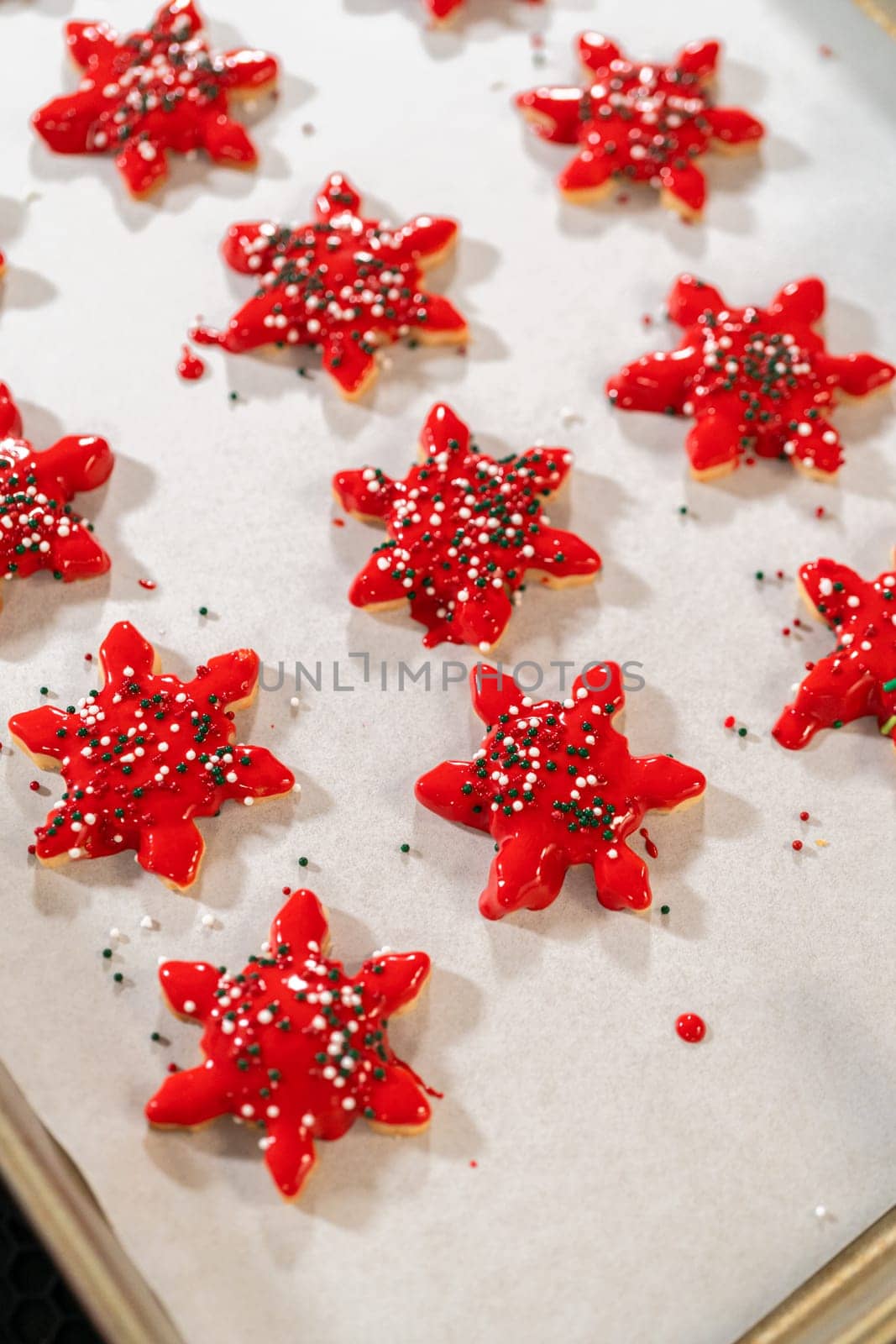 Vivid red star-shaped cookies, generously iced and speckled with green and white holiday sprinkles, freshly prepared and laid out to dry.