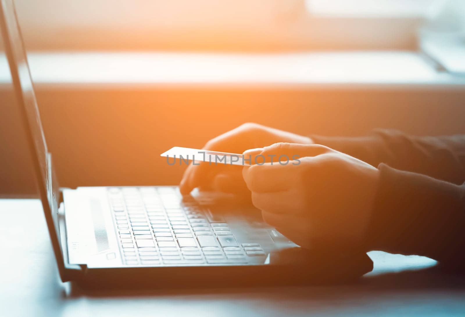 A man holds a bank card in his hand and types on a laptop keyboard, pays for purchases, makes online banking through an application, close-up view of his hands.