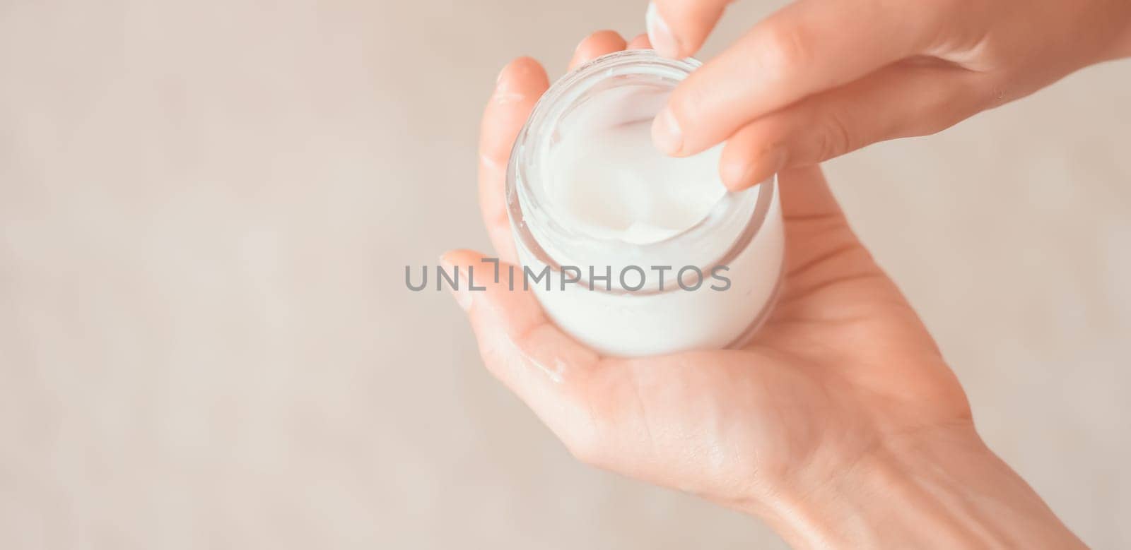 Young female hands hold a jar of moisturizing cream to maintain health, softness of the skin, the woman takes care of her health and beauty.