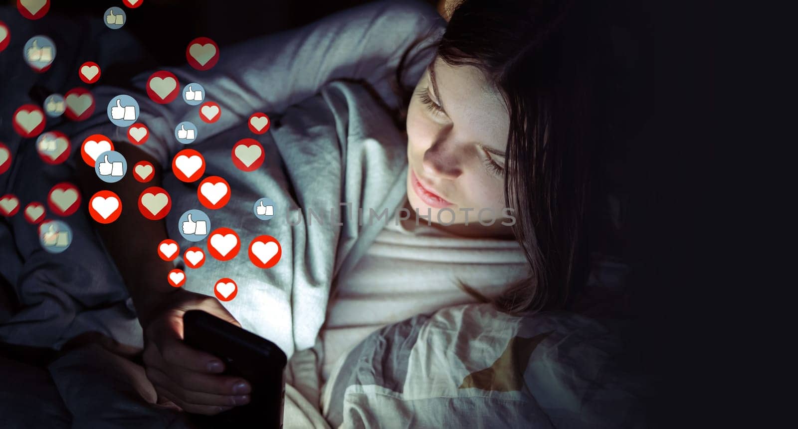 Young girl lies in bed at night with a mobile phone and sends or receives likes and hearts on social networks, a woman publishes news, the symbols of hearts and likes are added over image.