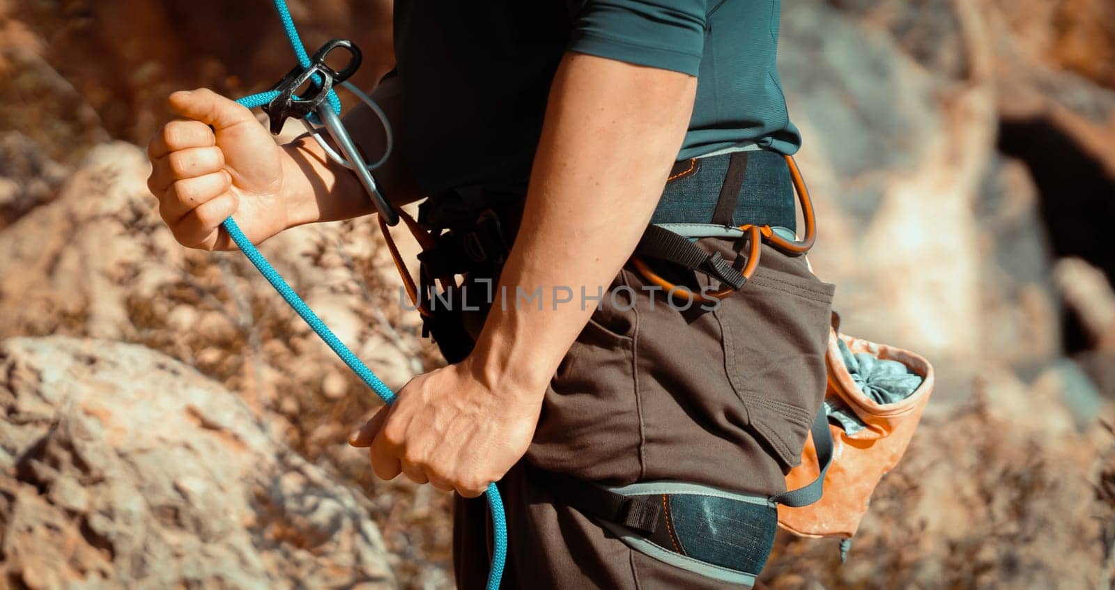 A young man belays for rock climbing in the mountains outdoors, an athlete controls on a rope during a workout, goes mountain climbing on a sunny day, close-up.