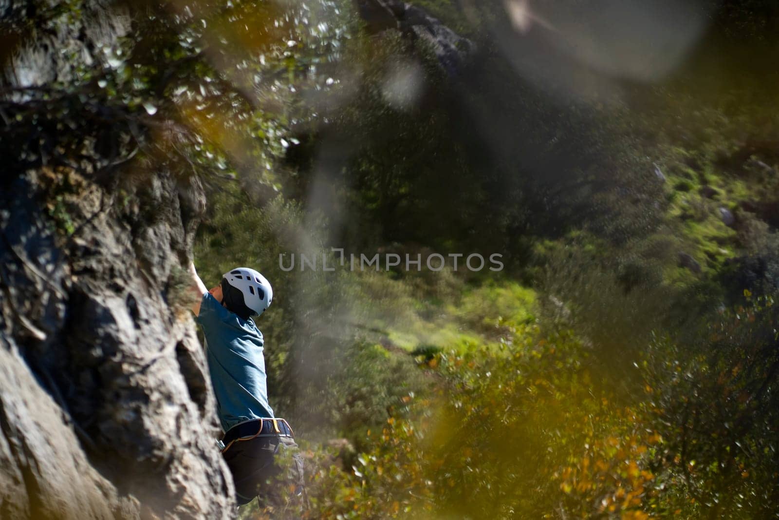 A young man is engaged in extreme sports, leads an active lifestyle, climbs a rock with climbing equipment in the sunny day against the background of Twin Caves, Leonidio, Arcadia, Greece.