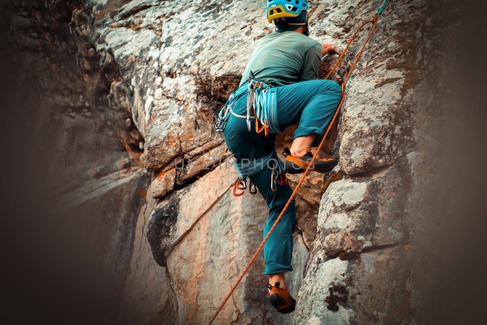 The young man is engaged in extreme sports, leads an active lifestyle, climbs a mountain, a rock with climbing equipment, wearing a helmet, with a rope, carabiners and climbing shoes.