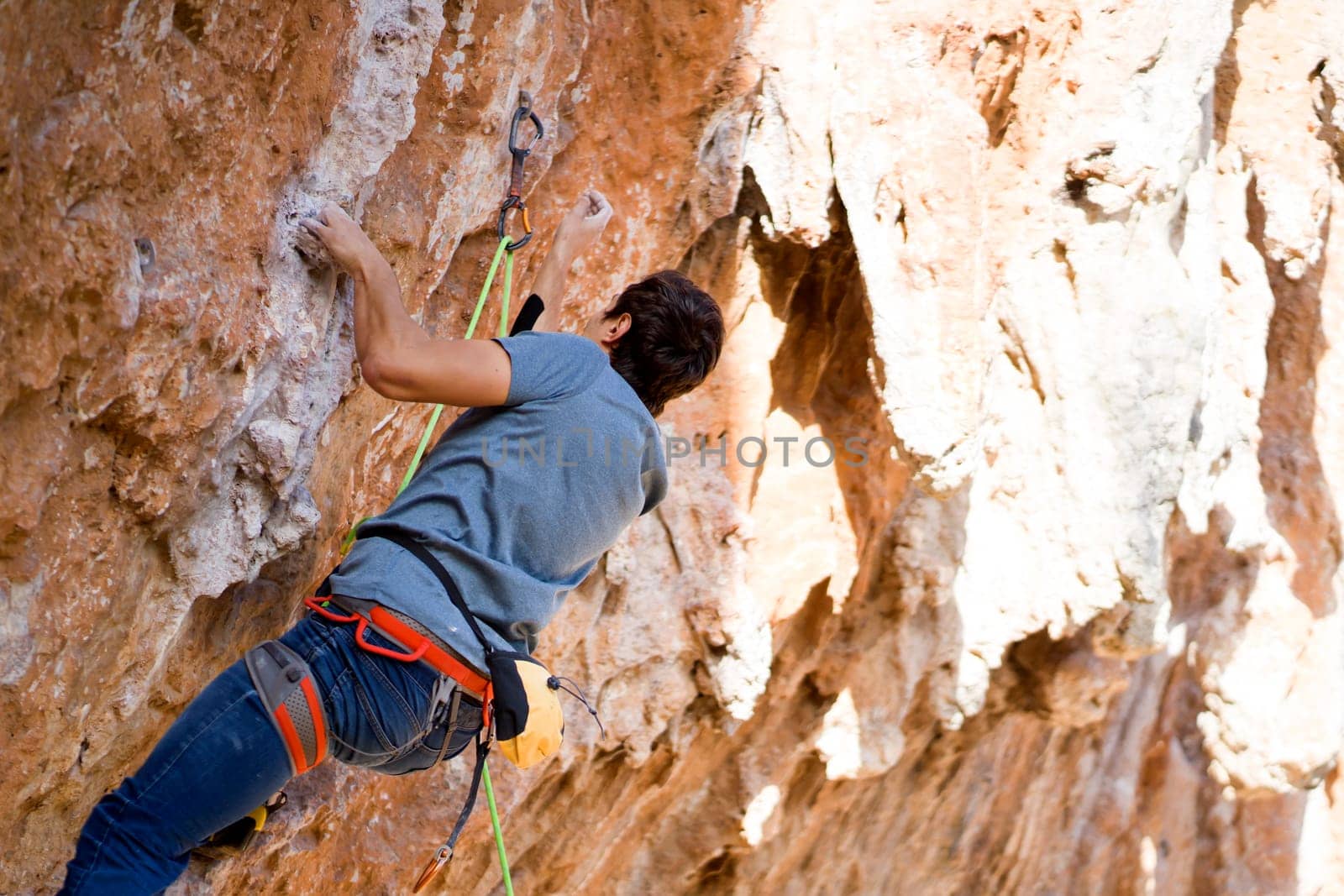A young man with climbing equipment, in rock shoes, with a rope, magnesia, climbs the mountain up, is involved in rock climbing, mountaineering, extreme active sports.