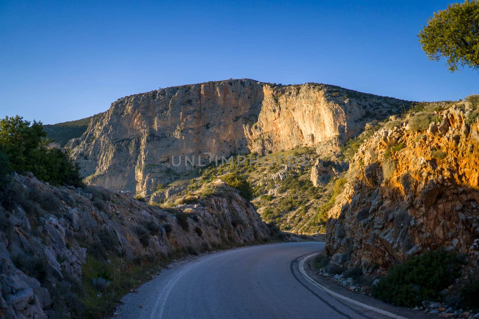 Beautiful road among the rocky yellow-red mountains on the southern mediterranean coast in the rays of the sun at sunset.